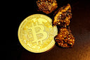 Gold bitcoin coin with intricate design and metallic sheen beside rough gold ore fragments in fine jewelry context