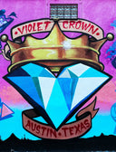 A vibrant mural of royal jewels features a gold crown and a large blue diamond with red banners in austin texas.