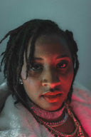 Woman with dreadlocks and jewelry illuminated by red light.