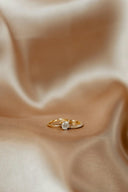 A delicate gold jewelry ring with a central round diamond and halo of smaller diamonds on beige satin