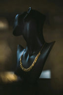 Gold jewelry featuring an intricate leaf-like art gold pendant displayed on a black mannequin bust