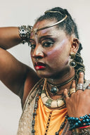 A woman wearing intricate gold and silver art gold jewelry including layered necklaces, a beaded headband, and multiple rings.
