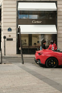 A vibrant red Ferrari sports car with black rims parked outside Cartier boutique symbolizing luxury jewelry allure.