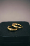 a pair of gold hoop earrings sitting on top of a black case
