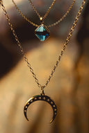 A delicate gold-toned crescent moon necklace with sparkling stones and a blue gemstone charm from everett jewelry store.