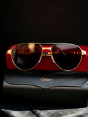 Gold-framed aviator sunglasses with dark lenses on a red Cartier box highlighting fine jewelry and art gold craftsmanship.