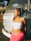 Woman with colorful beaded braids wearing a white crop top and pink skirt showcasing art deco and victorian gold style.