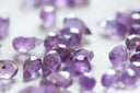 Faceted purple amethyst gemstones scattered on a light surface ideal for art gold and 18k gold jewelry designs