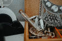 A silver intricately detailed necklace with hidden jewelry compartments rests on a wooden tray near engagement rings and cursed gems