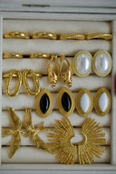 Gold jewelry featuring gold-toned earrings with pearl, black onyx accents, textured twists, bird motifs, and sunburst shapes