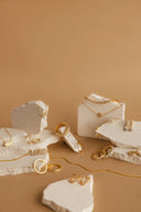 Gold jewelry collection with 18k gold delicate chains and fine jewelry rings displayed on white stone slabs