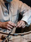 A craftsman in a van cleef lab coat carefully assembles fine jewelry components on a wooden workbench.