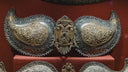 An ornate silver and gold metal belt buckle with floral engravings and a royal jewels double-headed eagle emblem with gemstone eye