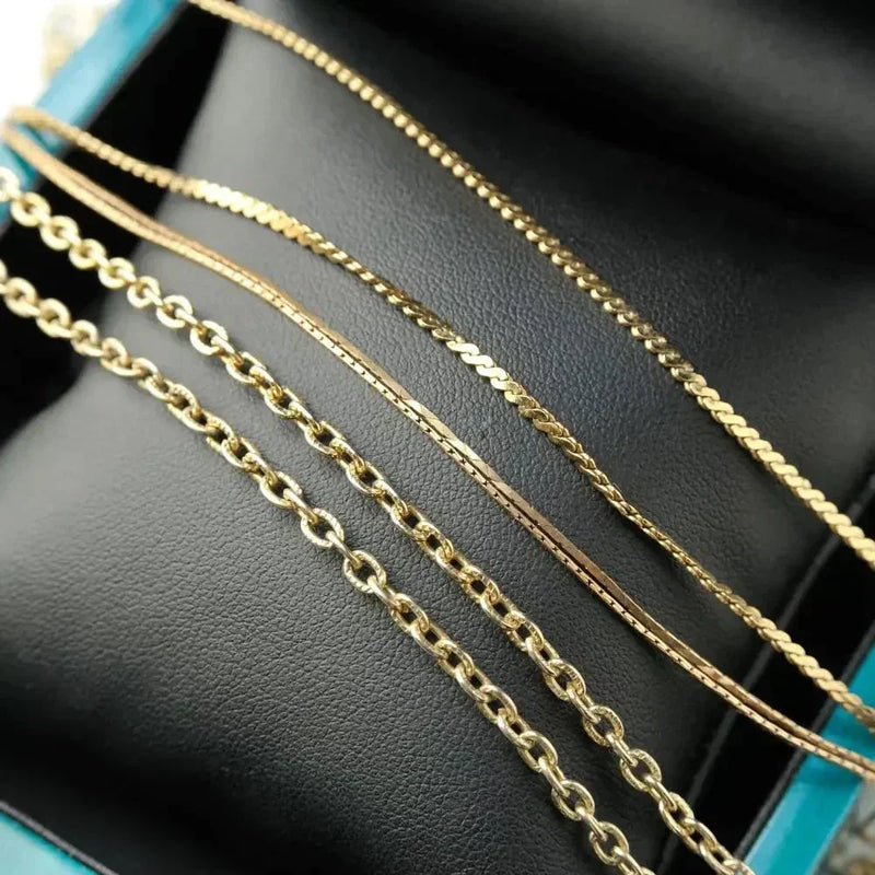 18k gold box chain and rope chain collection on dark surface