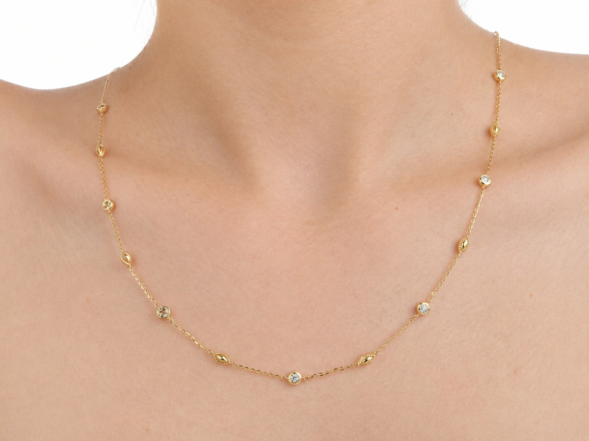 The diamond station necklace worn on the upper chest with the lowest station below the collarbone, the yellow gold chain against bare skin