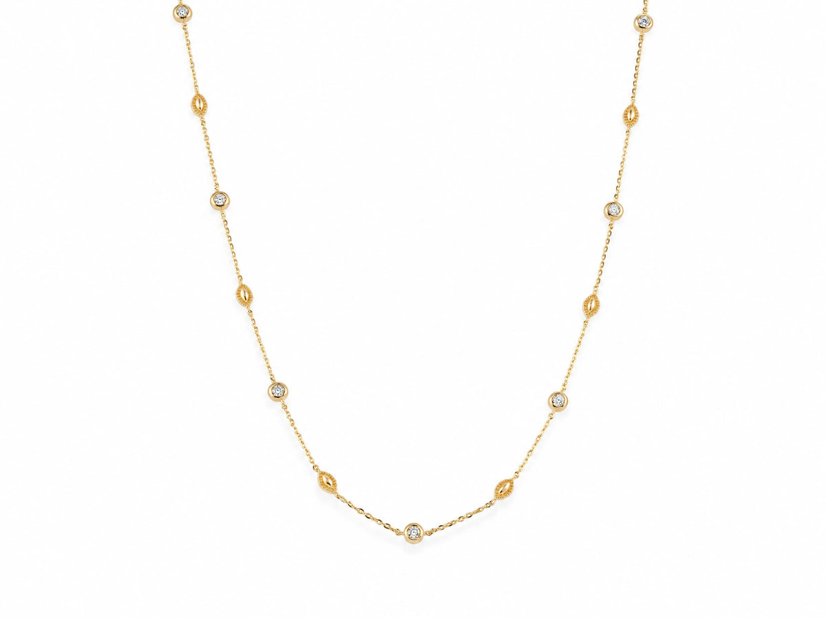 14K yellow gold station necklace laid out on white, round diamonds in gold bezels alternating with milgrain gold beads along the fine cable chain