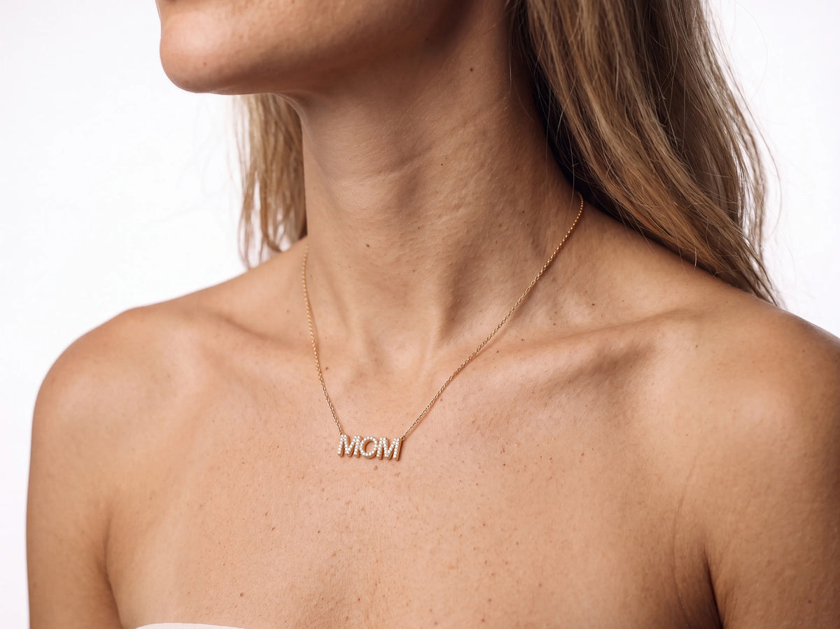 The MOM pendant worn on the upper chest below the collarbone, the yellow gold chain against bare skin, the jaw at the top edge of the frame