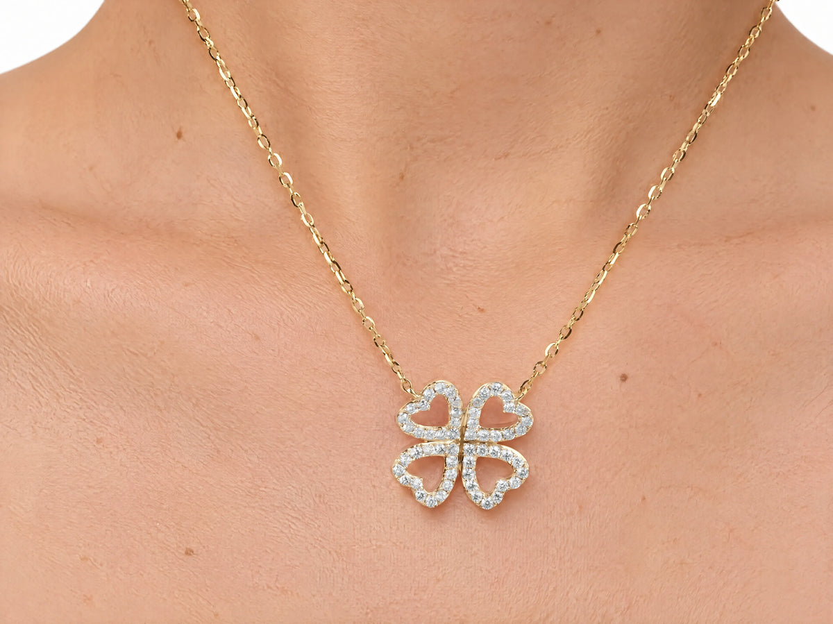 The clover pendant worn on the upper chest just below the collarbone, the yellow gold chain against bare skin