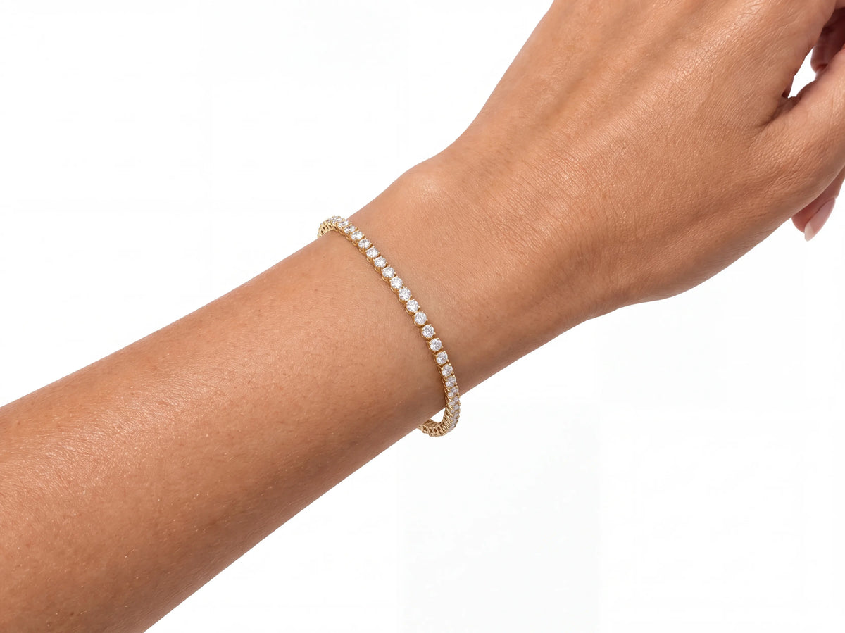 The tennis bracelet on a wrist seen close, the stone row face-on and the gold settings in profile where the bracelet lifts away