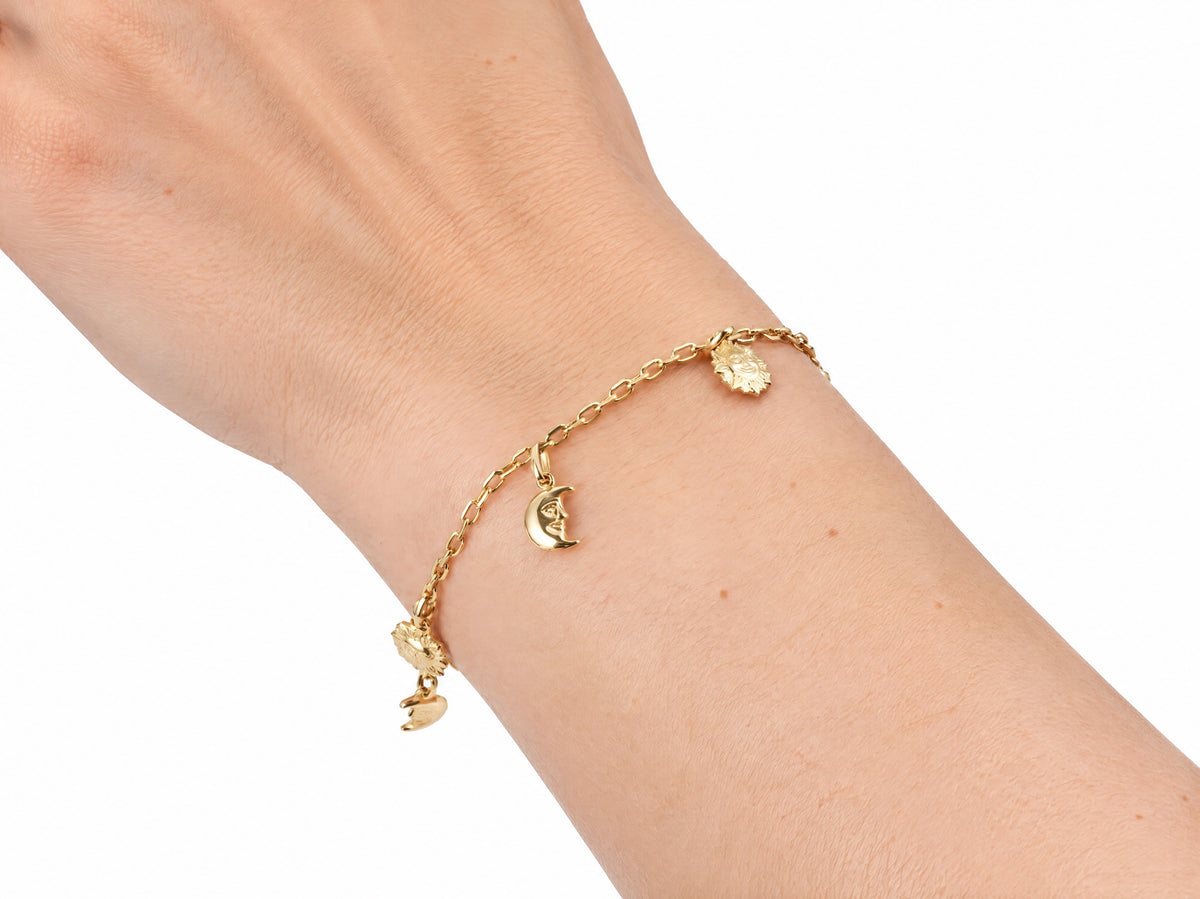 Gold charm bracelet worn on the wrist with the sun and moon charms visible