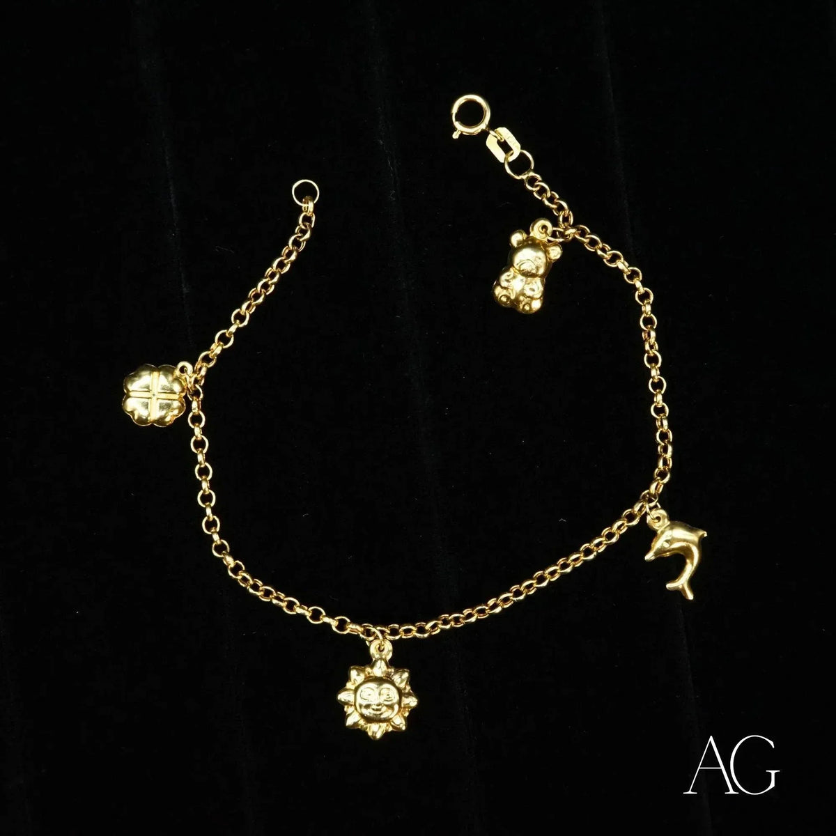 18k gold charm bracelet with teddy bear, dolphin, sun, and clover charms on black background