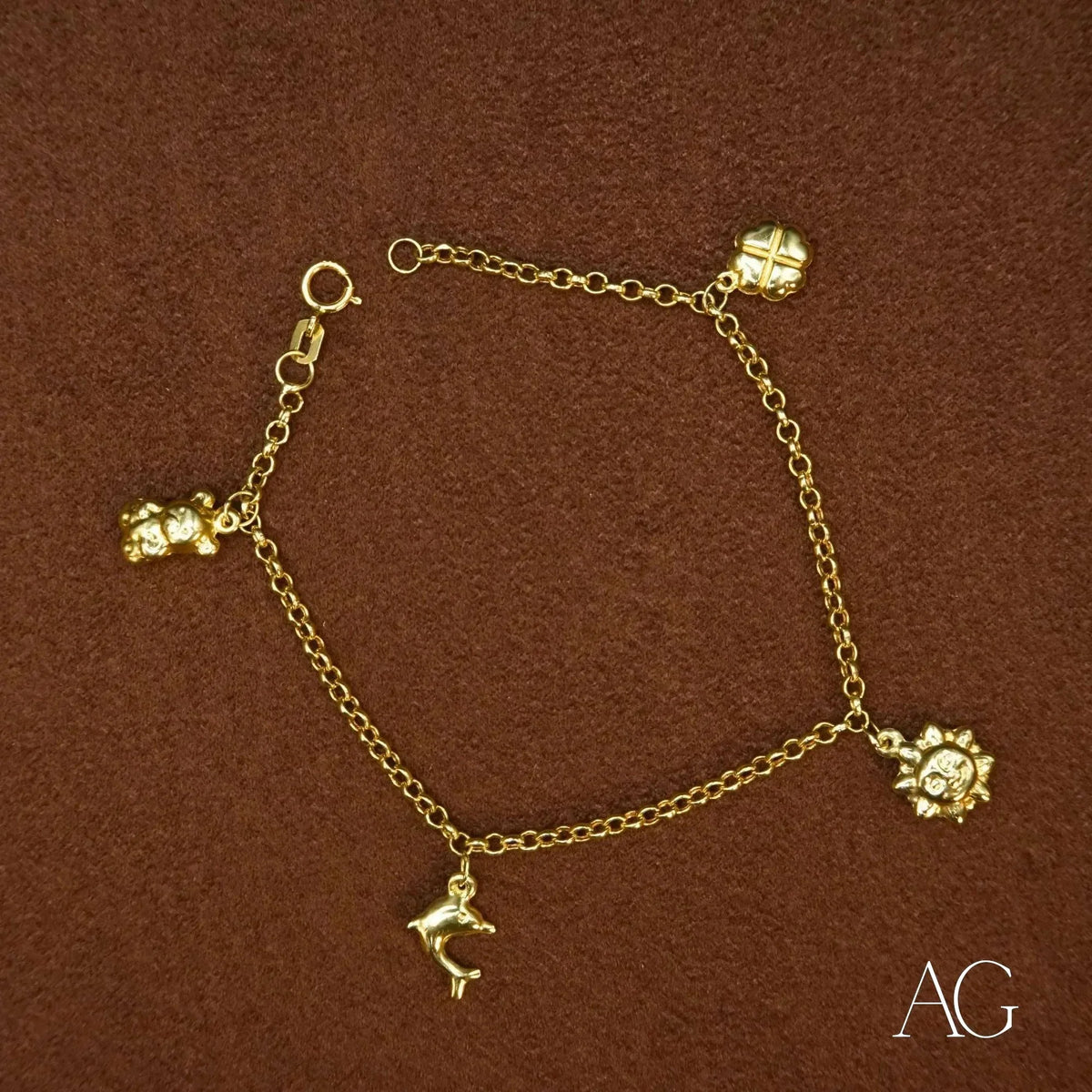 18k gold charm bracelet with teddy bear, dolphin, sun, and clover charms on brown surface