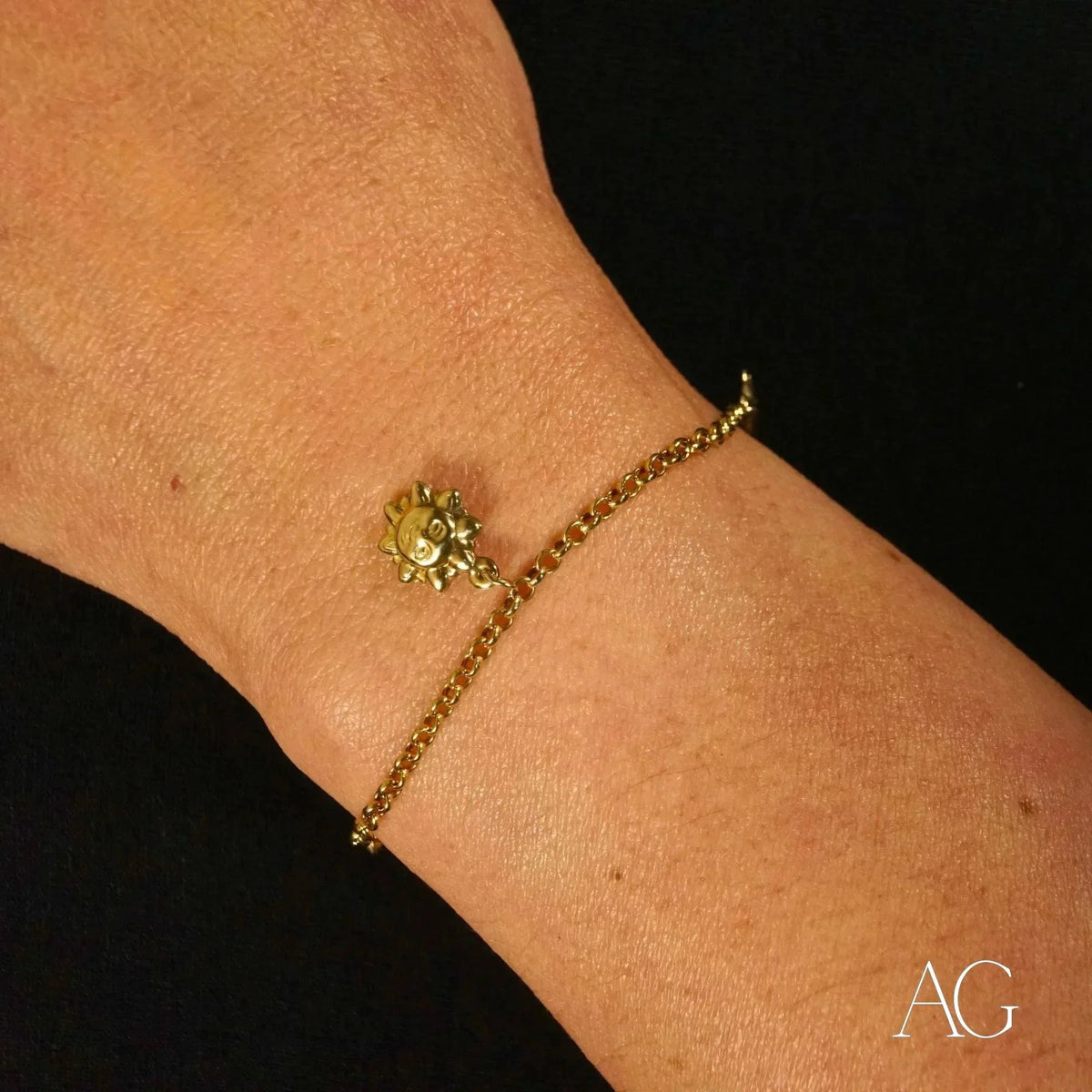Close-up detail of 18k gold charm bracelet featuring sun charm and chain links