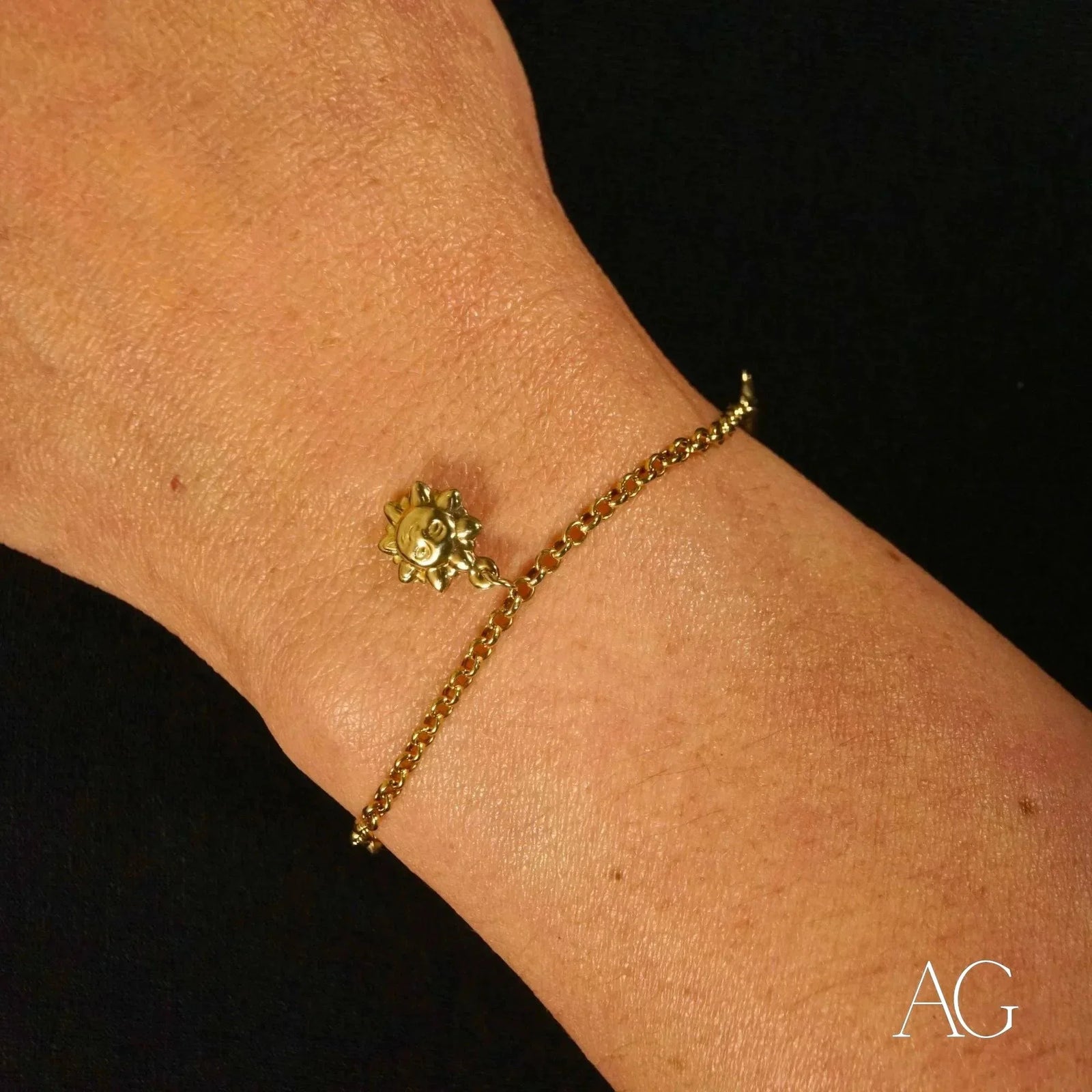 Close-up detail of 18k gold charm bracelet featuring sun charm and chain links