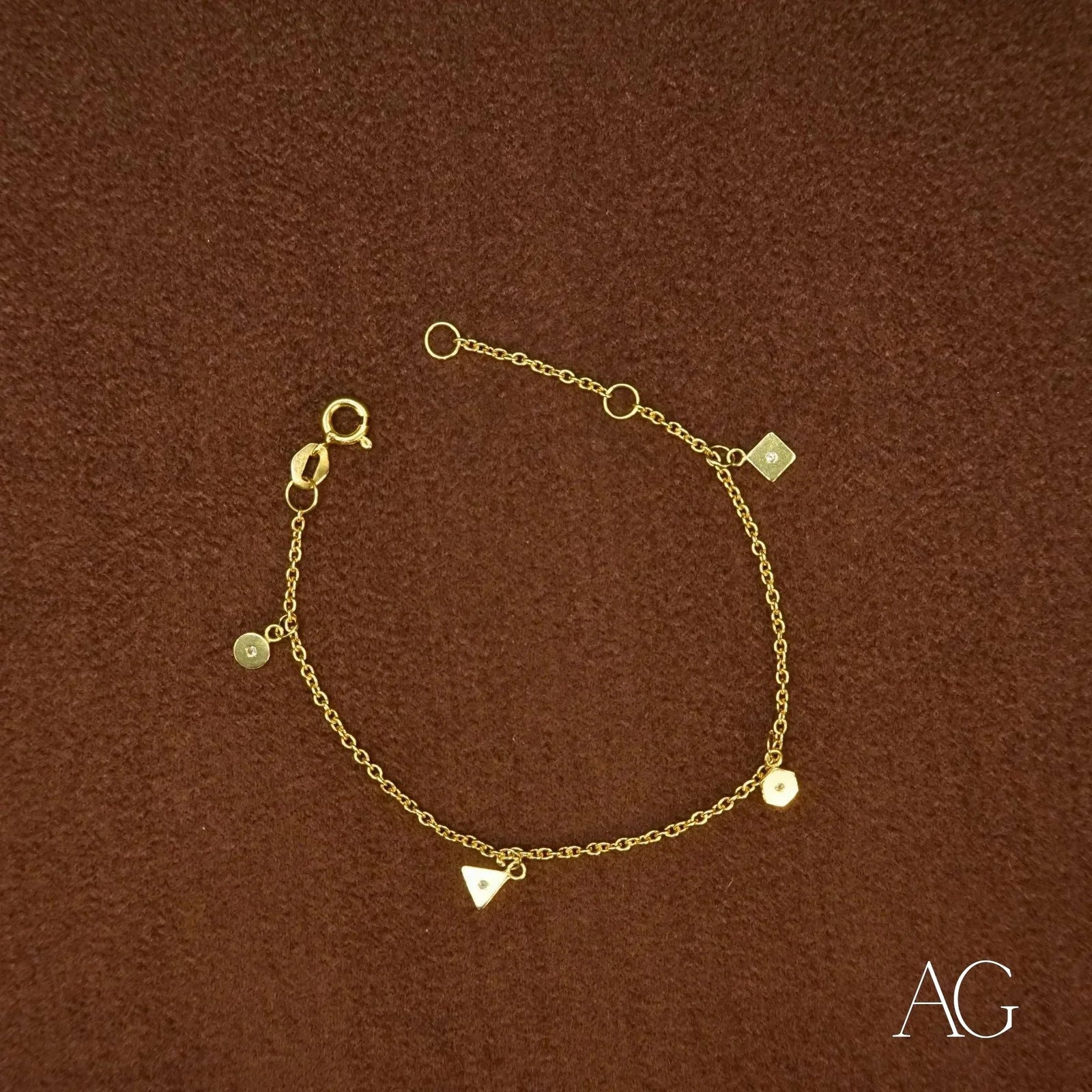 18K gold charm bracelet with triangular, hexagonal, square and circular clear stone charms on brown background