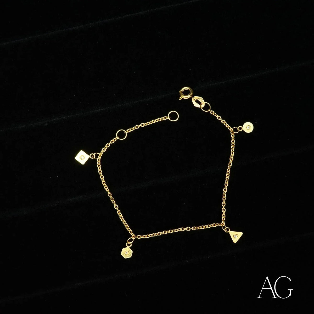 18K gold bracelet with square, triangle, hexagon and circular charms on delicate chain, black background