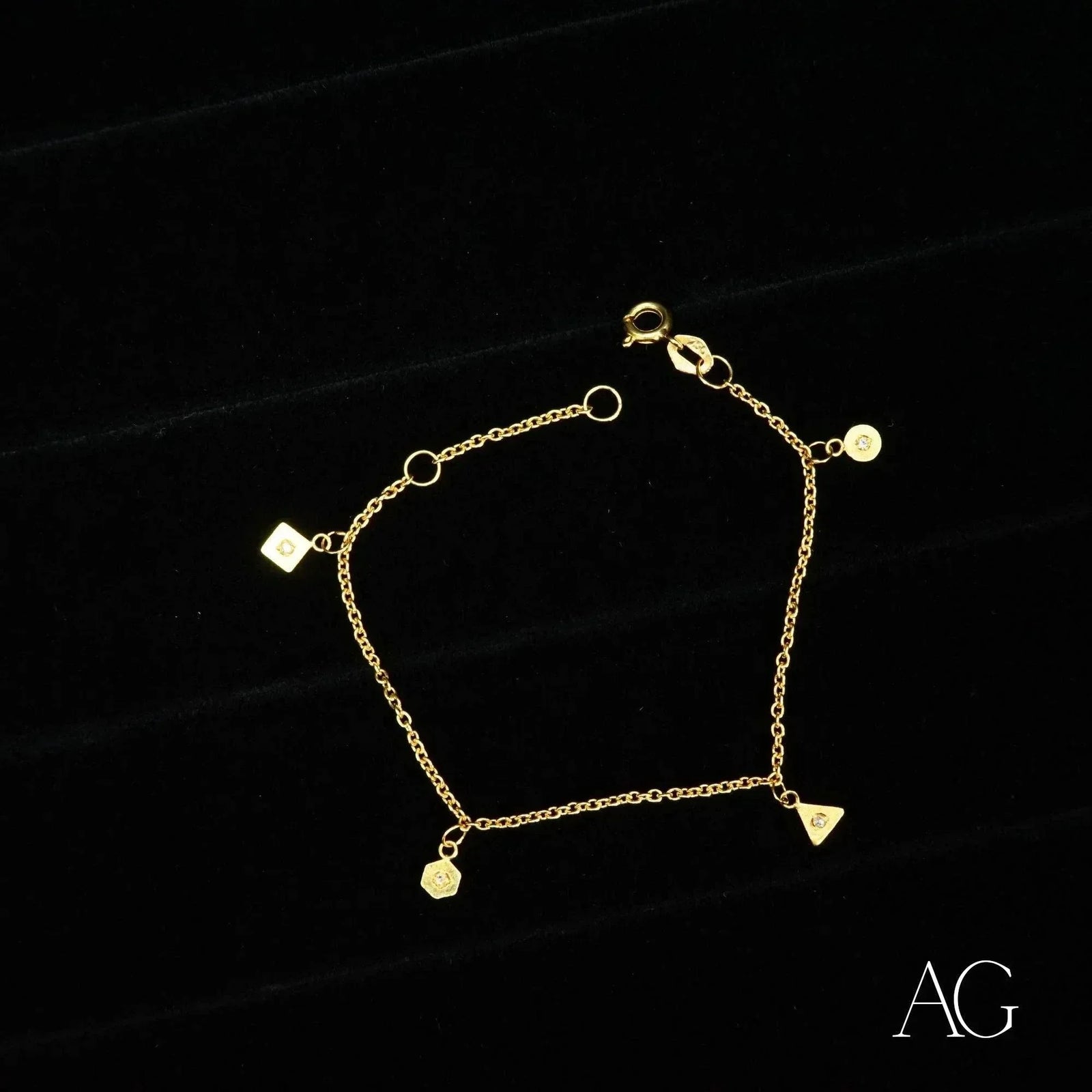 18K gold bracelet with square, triangle, hexagon and circular charms on delicate chain, black background