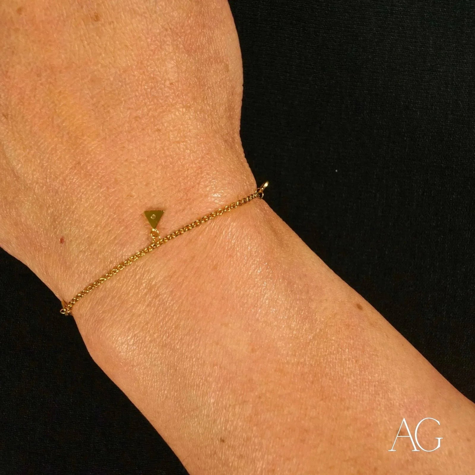 Close-up detail of 18K gold bracelet chain with triangular charm set with clear stone
