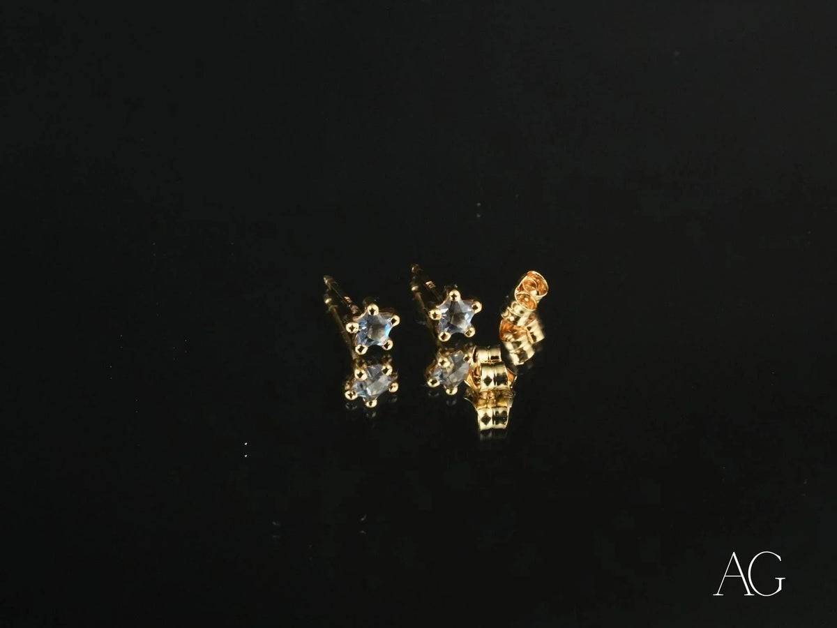 Two 18K gold stud earrings with blue stones on reflective black surface