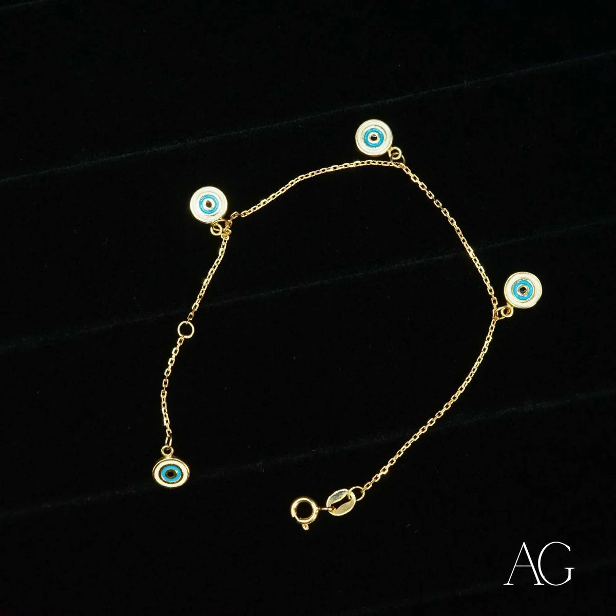 18k gold evil eye bracelet for kids with four dangling blue and white enamel charms, flat lay on black background