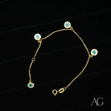18k gold evil eye bracelet for kids with four dangling blue and white enamel charms, flat lay on black background