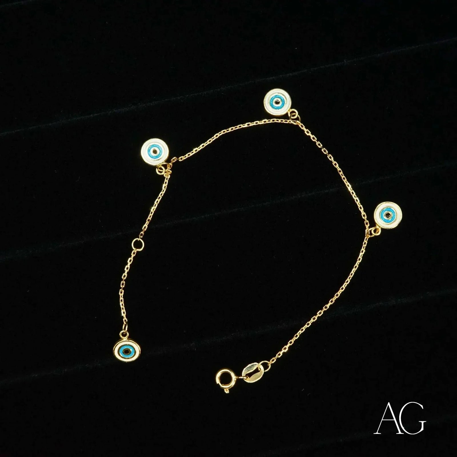 18k gold evil eye bracelet for kids with four dangling blue and white enamel charms, flat lay on black background