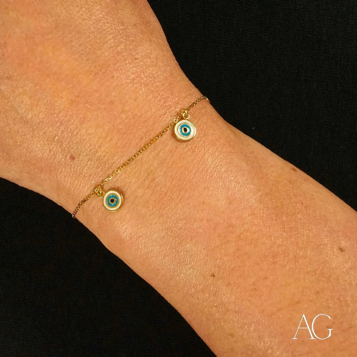 18k gold evil eye bracelet for kids with two dangling blue and white enamel charms, close-up view