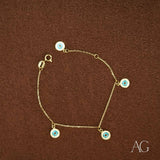 18k gold evil eye bracelet for kids with five dangling blue and white enamel charms, top-down view on brown surface