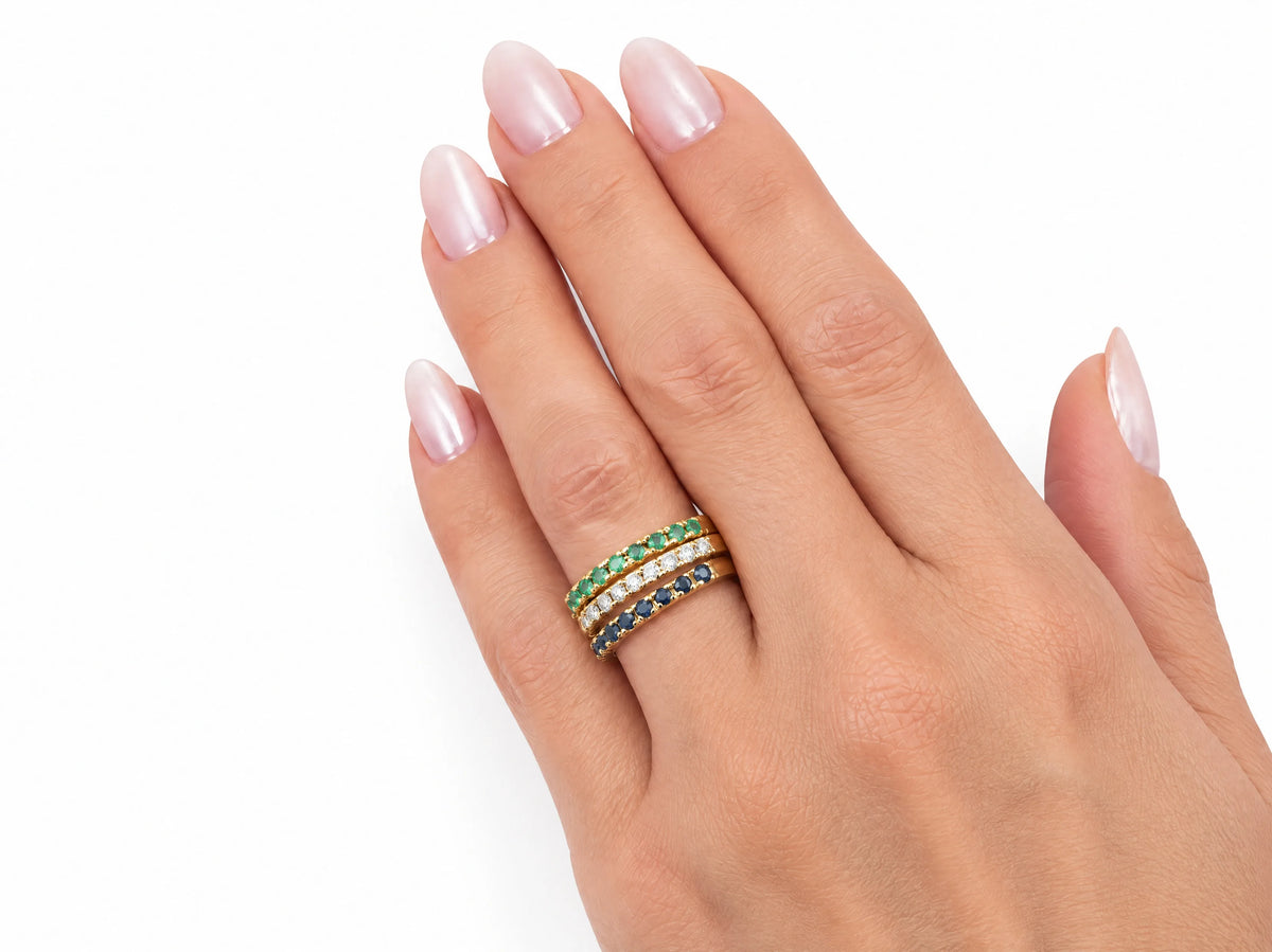 ArtGold 18K yellow gold half eternity bands worn together on the finger, close view of the diamond, emerald and sapphire rows