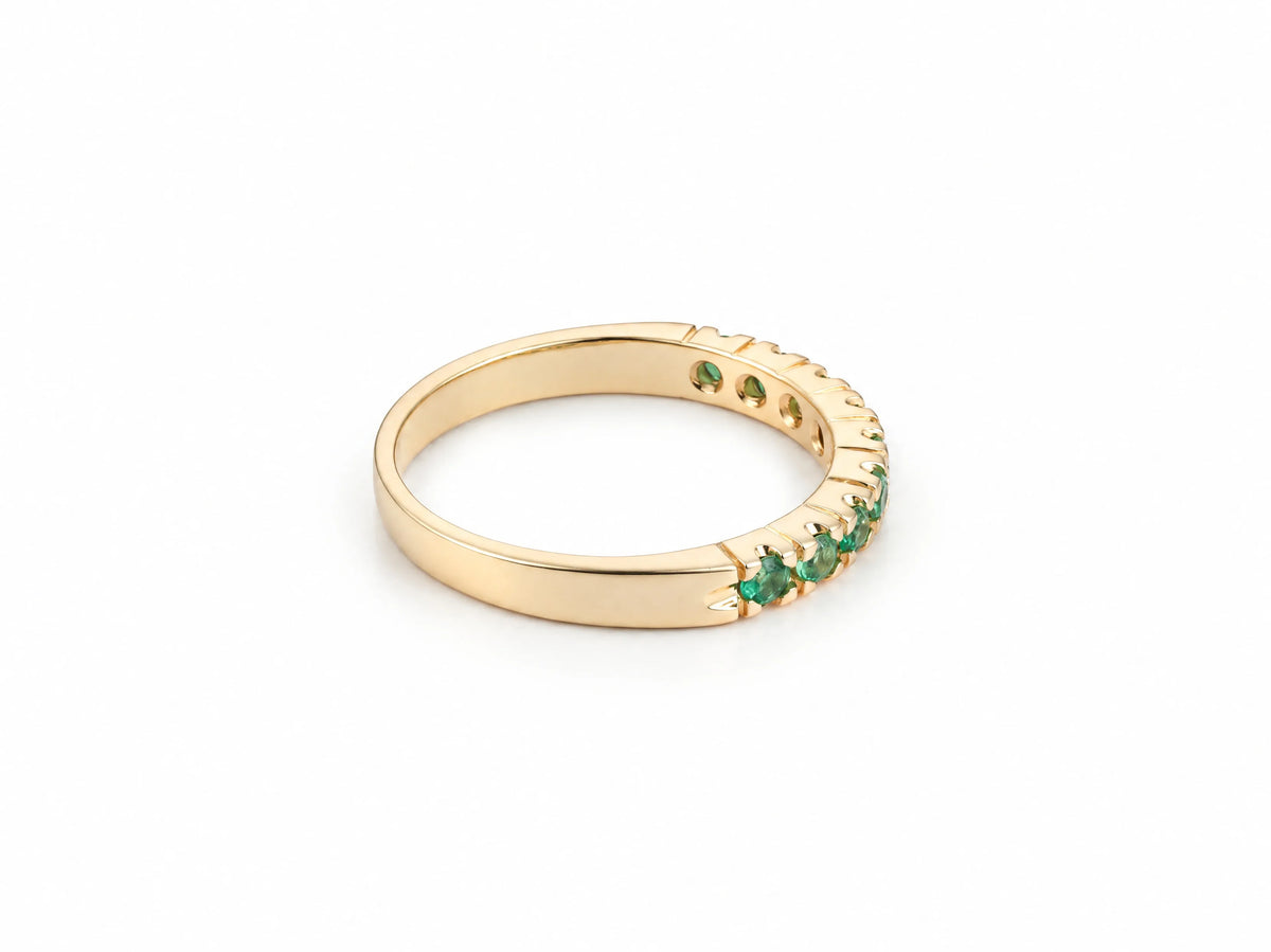 ArtGold 18K yellow gold half eternity emerald band, three-quarter view showing the row of nine round green emeralds and the smooth plain back of the band