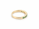 ArtGold 18K yellow gold half eternity emerald band, three-quarter view showing the row of nine round green emeralds and the smooth plain back of the band