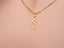 Close-up shot of the 18 k gold cat pendant on a chain against a pink background, highlighting the polished finish and delicate shape.