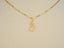 The solid 18 k gold cat pendant lying on a beige surface, emphasizing the polished finish and fine outline.