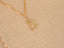 Full view of the 18 k gold cat pendant on a chain, shown on a beige fabric background, highlighting its petite size and warm gold color.
