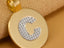 Macro detail of 18 K gold Celestia initial disc with white-gold “C” on beige cashmere—luxury red-carpet look like Taylor Swift.