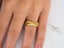 Gold textured 18k gold wedding band ring with classic fit worn on a finger