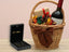 Golden Signature Necklace in an elegant jewelry box next to a gift basket with a bottle of wine and wrapped presents.