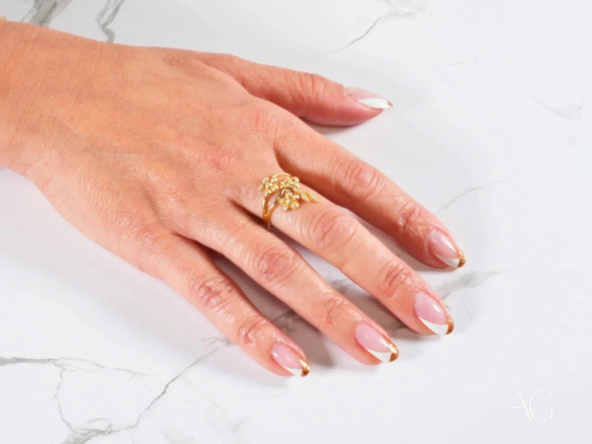 Womans hand with French-tipped nails wearing Blossom Charm 18k gold ring with diamond centerpiece