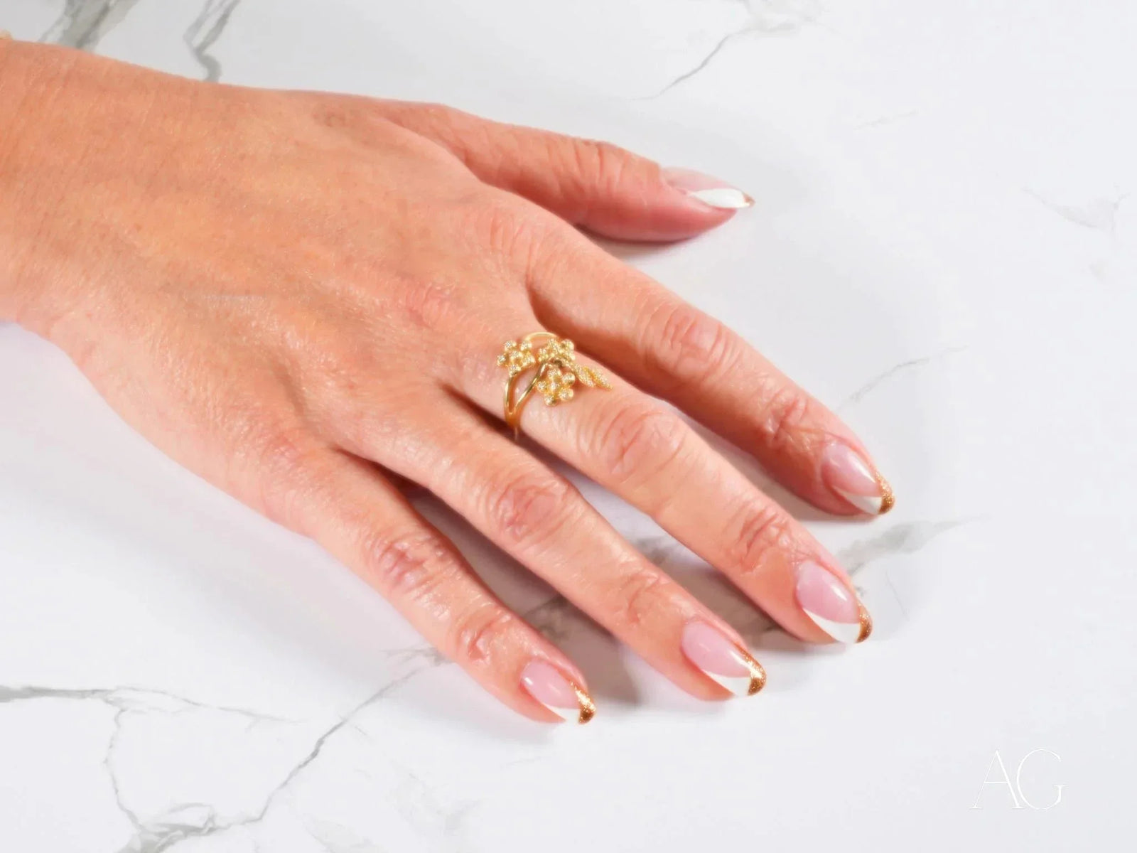 Womans hand with French-tipped nails wearing Blossom Charm 18k gold ring with diamond centerpiece