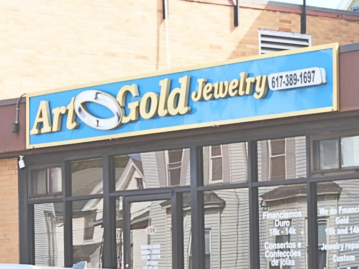 Blue and gold ’art gold jewelry’ storefront sign with a stylized silver ring logo.